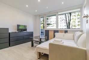 A modern hotel room with a bed, a TV, a desk, and a window with a city view.