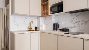 A modern kitchen with marble countertops, a built-in microwave, a coffee maker, and a gold faucet. - Tamka Powiśle Superior Studio (Warszawa)