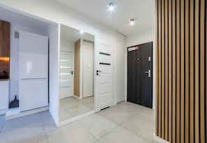 Ein modernes Interieur mit einem weißen Kühlschrank, einem Holzschrank, einer Tür mit Spiegel und einer schwarzen Tür mit einem Schild.