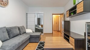 Ein modernes Wohnzimmer mit einem grauen Ecksofa, einem Holztisch, einem TV-Schrank und einer eingebauten Garderobe.
