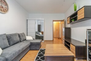 Ein modernes Wohnzimmer mit einem grauen Ecksofa, einem Holztisch, einem TV-Schrank und einer eingebauten Garderobe.
