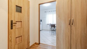 Eine Holztür mit kleinem Fenster und Griff, die in einen Raum mit Fliesenboden und einem Essbereich mit Stühlen und Tisch führt.