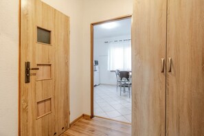 Eine Holztür mit kleinem Fenster und Griff, die in einen Raum mit Fliesenboden und einem Essbereich mit Stühlen und Tisch führt.
