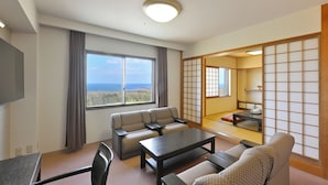 A hotel room with a sofa, a table, a chair, a TV, and a view of the ocean. - Livemax Resort Kanonji (Kanonji)