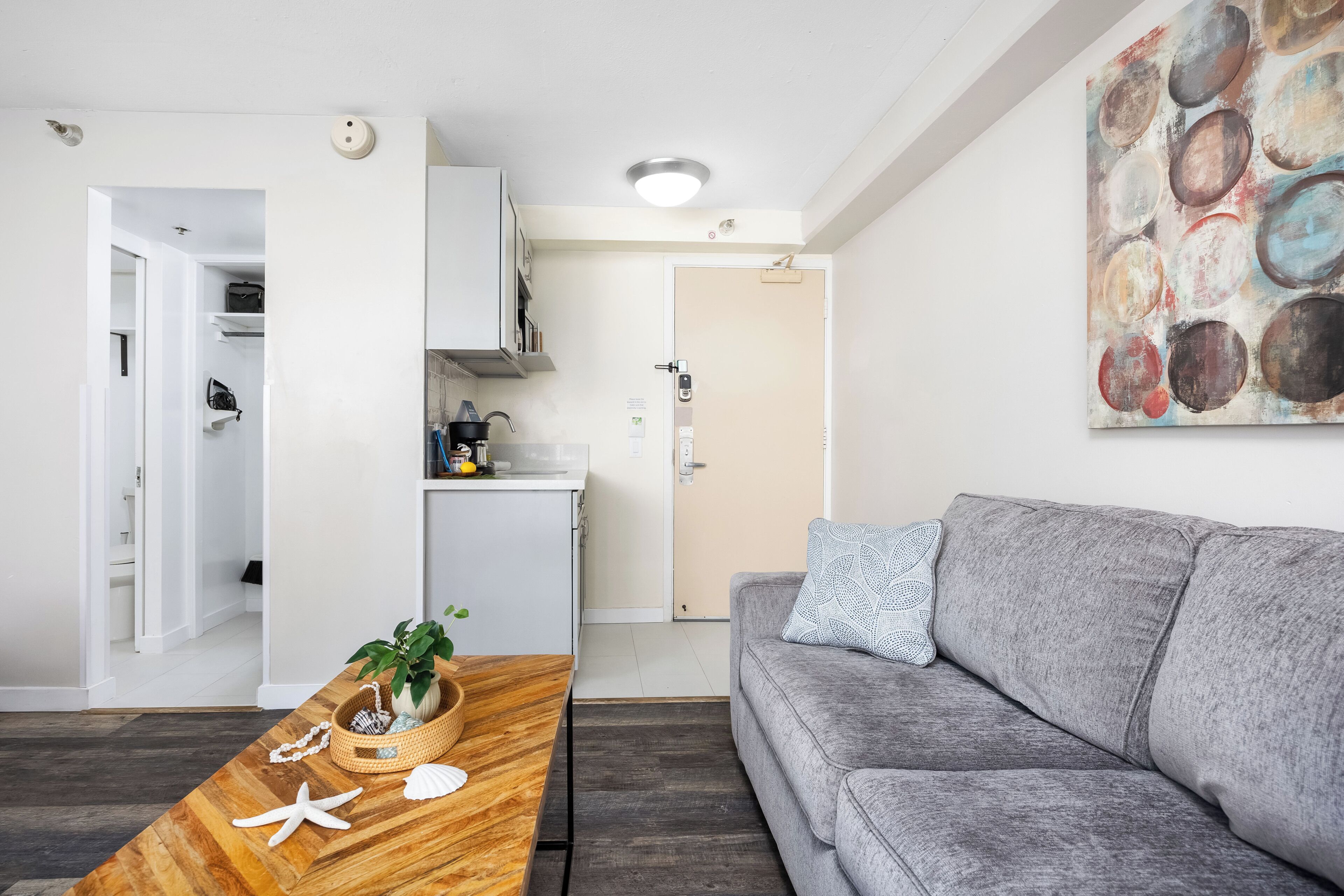 A modern living room with a grey sofa, wooden coffee table with decorative items, and a kitchen area in the background.