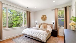 Een slaapkamer met een groot bed, twee bedlampen, een decoratief wandobject en uitzicht op groen buiten.