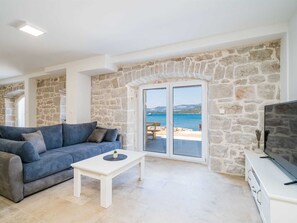 A living room with a stone wall, a sofa, a coffee table, and a television. - Beachfront Villa Olive Mill with pool by Interhome (Putniković)