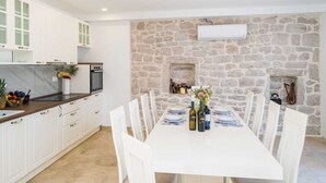 A modern kitchen with white cabinets, a stone wall, and a dining area with a white table set for six. - Vacation home  by Interhome (Putniković)