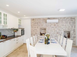 Eine moderne Küche mit weißen Schränken, einer Steinwand und einem Essbereich mit weißem Tisch, gedeckt für sechs Personen.