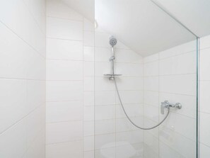 Um chuveiro com um chuveiro manual e uma torneira fixa em um quarto revestido com azulejos.