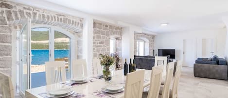 Un salon moderne avec un mur en pierre, un coin repas avec une table dressée pour quatre personnes et une vue sur la mer.