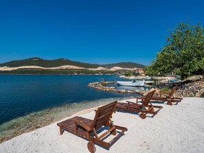 A beach with clear water, wooden lounge chairs, and boats. - Beachfront Villa Olive Mill with pool by Interhome (Putniković)