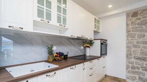 A modern kitchen with white cabinetry, a marble backsplash, a wooden countertop, and a stone wall. - Vacation home  by Interhome (Putniković)