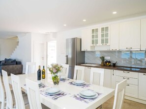 A modern kitchen with white cabinetry, a stainless steel refrigerator, and a dining area with white chairs and a table set for two. - Beachfront Villa Olive Mill with pool by Interhome (Putniković)