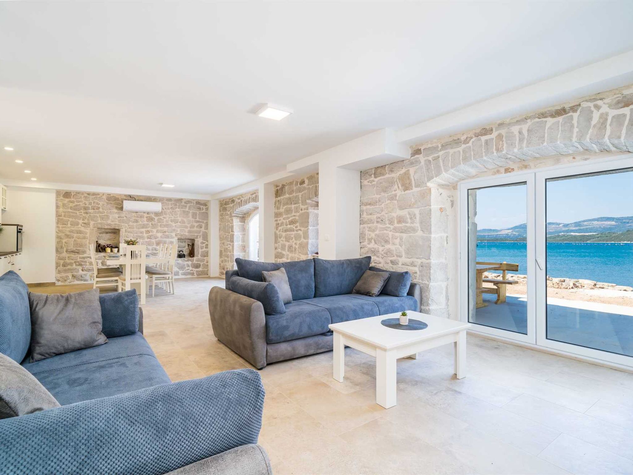 Ein modernes Wohnzimmer mit Steinwänden, einem großen Fenster mit Meerblick und einer Sitzecke mit Sofas und einem Couchtisch.