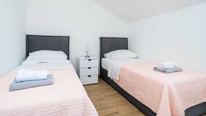 A bedroom with two beds, each with a pillow and a folded towel. There is a nightstand with a lamp between the beds. - Vacation home  by Interhome (Putniković)