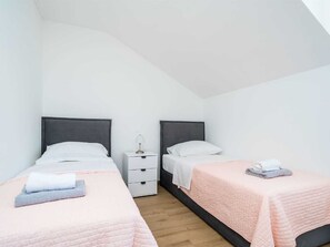 Ein Schlafzimmer mit zwei Betten, jeweils mit Kissen und einem gefalteten Handtuch. Zwischen den Betten steht ein Nachttisch mit einer Lampe.