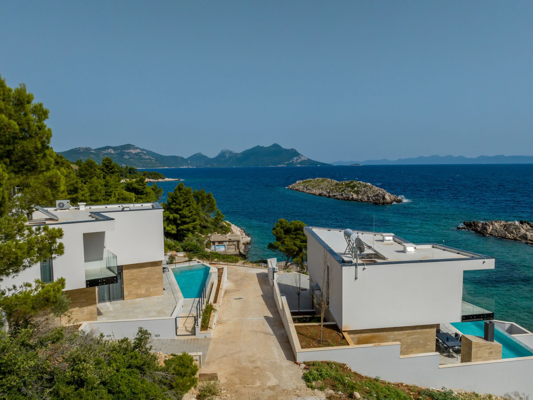 Une villa moderne dotée d’une piscine, offrant une vue imprenable sur une mer d’un bleu profond et sur des montagnes lointaines.