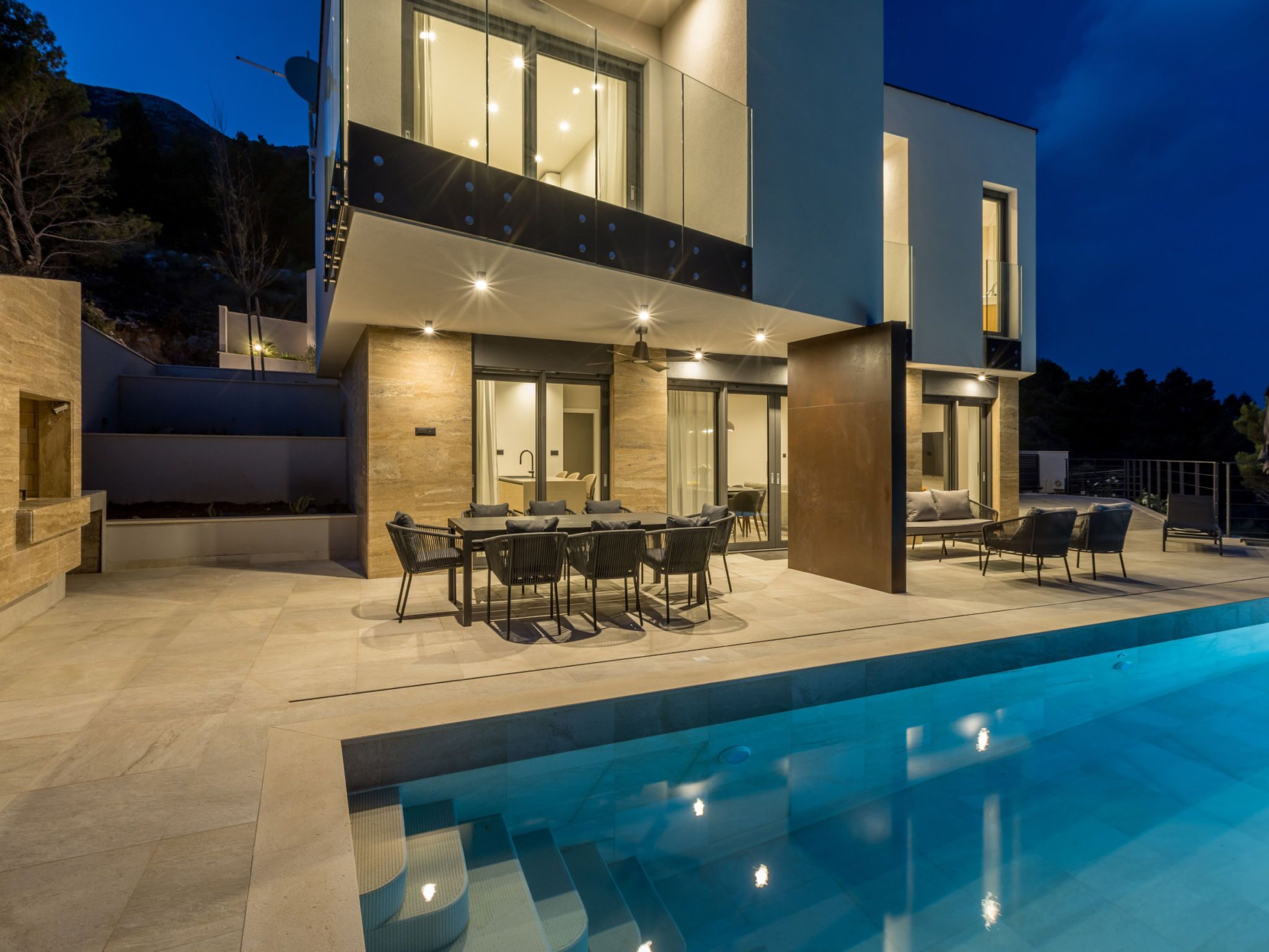 Una casa moderna de dos pisos con piscina, mobiliario exterior y un patio bien iluminado.