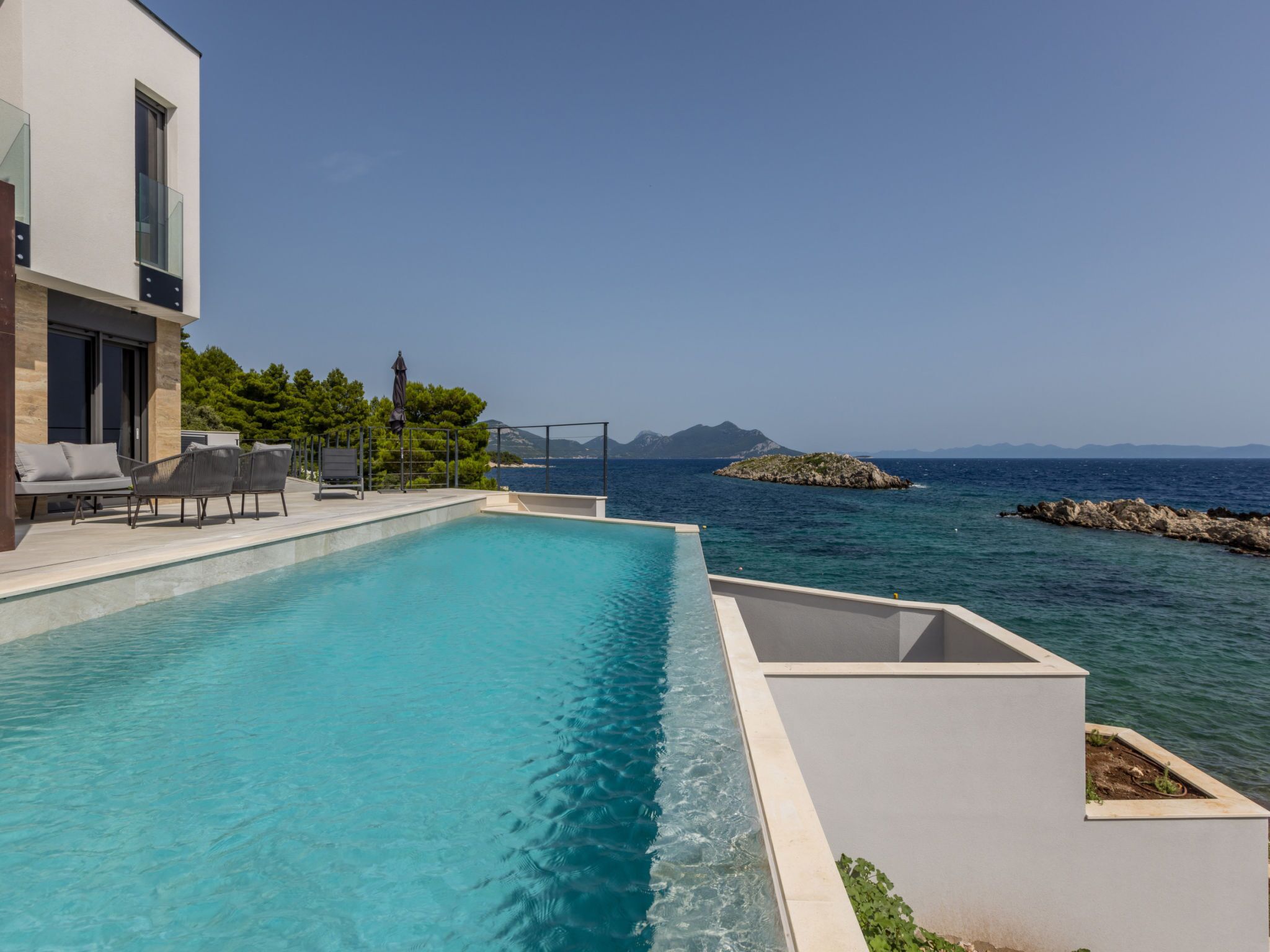 A modern pool with clear blue water, surrounded by a white deck and lounge chairs.