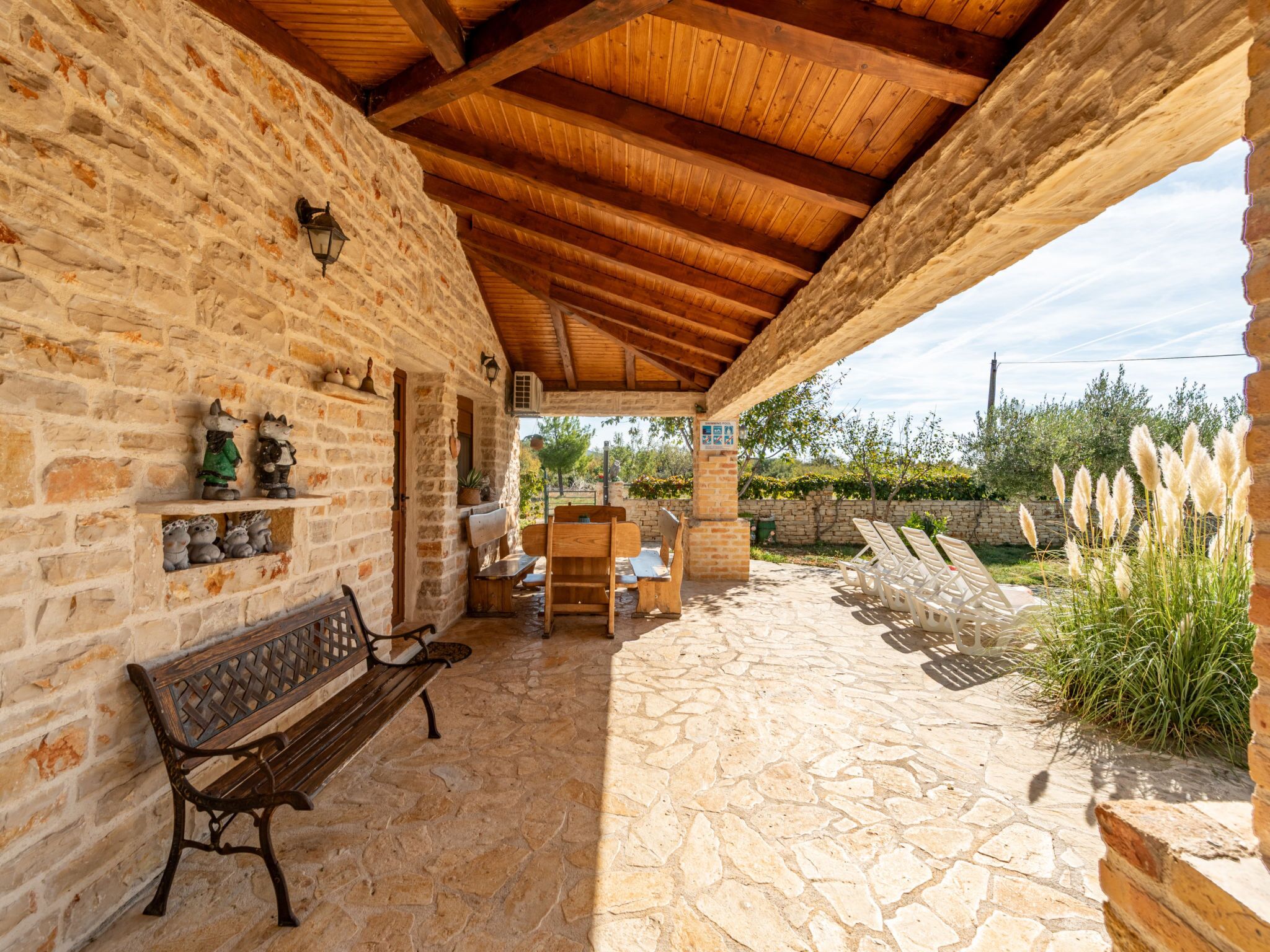 Un patio de piedra con un banco de madera y una mesa, un muro de piedra decorado con objetos, y vistas del paisaje circundante.