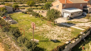 Zona residencial amb una casa gran, teulada a rajola, carrer d'accés pavimentat i pati tancat amb un trampolí i jocs infantils.