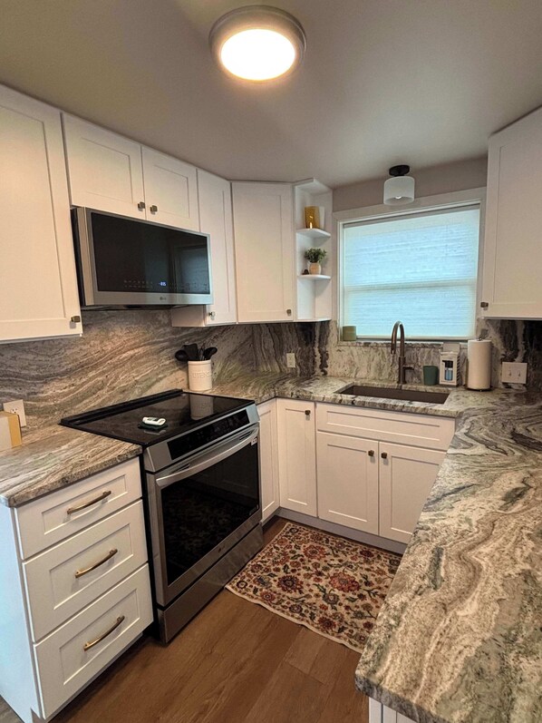 A modern kitchen with white cabinets, a black stove, a microwave, and a marble countertop.