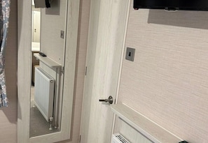 Une pièce avec une porte en bois, un radiateur, un miroir et un thermostat.