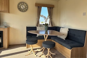A compact living space with a round table, two stools, a sofa, and a clock on the wall.