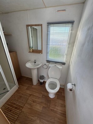 A compact bathroom with a sink, toilet, and window. - Cabin Sleeps 8 with Indoor Pool (Rhyl)