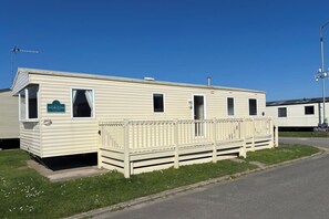 A single-story mobile home with a fenced front yard, a small porch, and a clear blue sky.