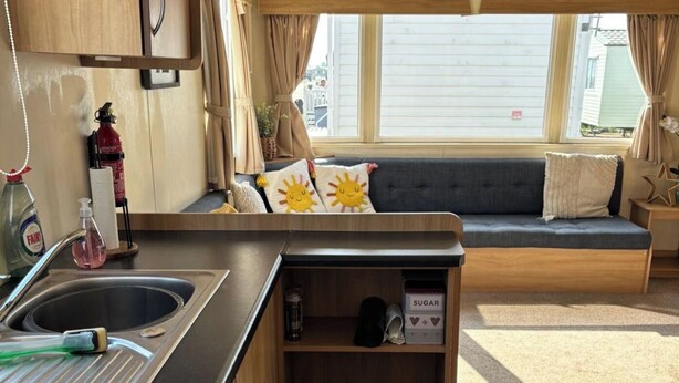 Un intérieur de camping-car compact comprenant un coin cuisine, un espace salon avec des coussins et une fenêtre offrant une vue sur l’extérieur.