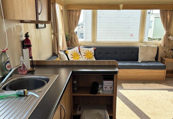 A compact RV interior with a kitchenette, a seating area with cushions, and a window providing a view of the outside.