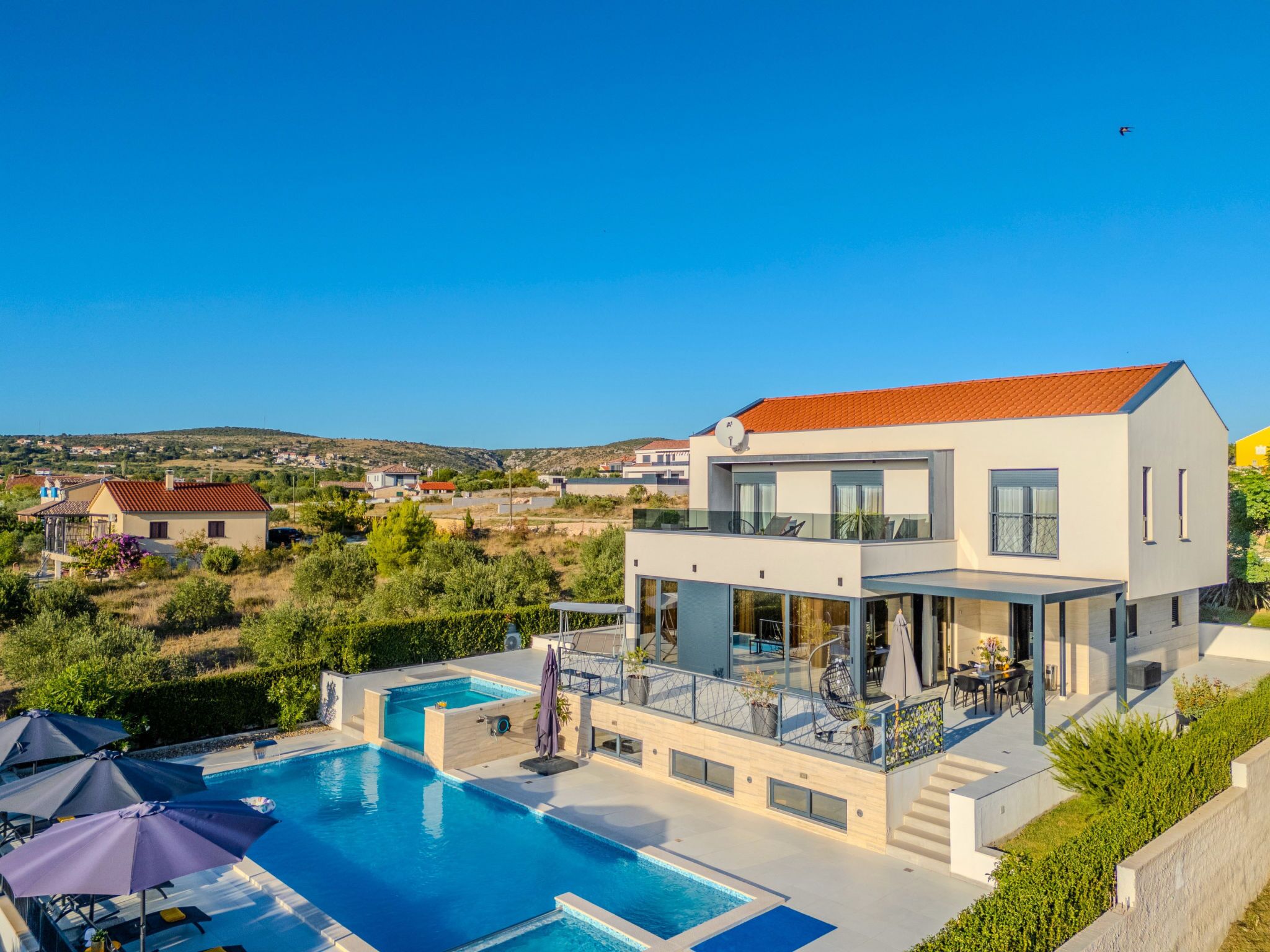 A modern two-story house with a swimming pool, outdoor seating, and a view of the surrounding landscape.