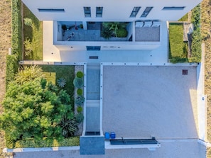 Vista aérea de un edificio moderno con un patio central, rodeado de abundante vegetación y una zona pavimentada.