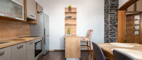 Cocina compacta con horno integrado, refrigerador y mesa de madera con sillas.