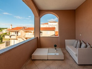 A balcony with a sofa and a small table, a view of neighboring buildings, and a clear sky. - Apartment  by Interhome (Biograd na Moru)