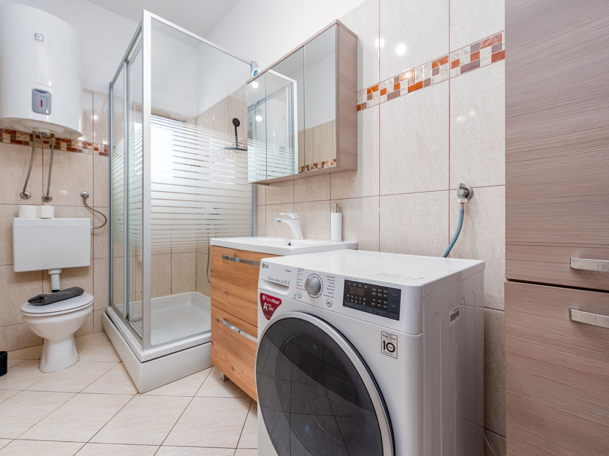 A modern bathroom with a glass shower enclosure, a built-in washing machine, and a toilet.