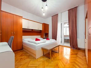 A hotel room with a wooden floor, a bed with white bedding and red accents, a bench, a desk, and a wardrobe. - Apartment Julia A6, 4+2 by Interhome (Biograd na Moru)