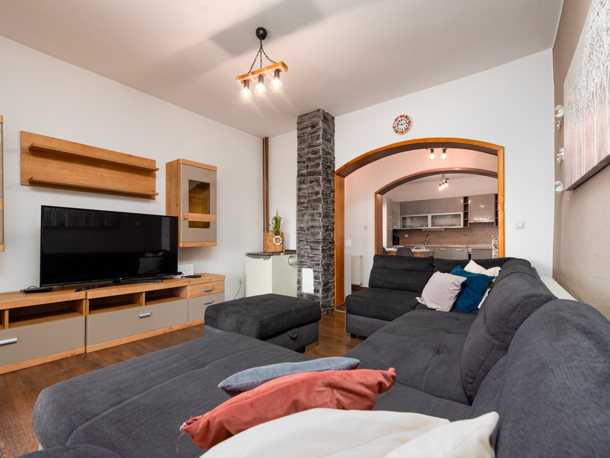 Ein modernes Wohnzimmer mit einem Flachbildfernseher, einer Wand aus Stein und einer gemütlichen Sitzecke mit Kissen.