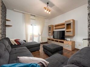 A modern living room with a grey sofa set, a flat-screen TV, wooden shelving, and a stone accent wall. - Apartment Julia A6, 4+2 by Interhome (Biograd na Moru)