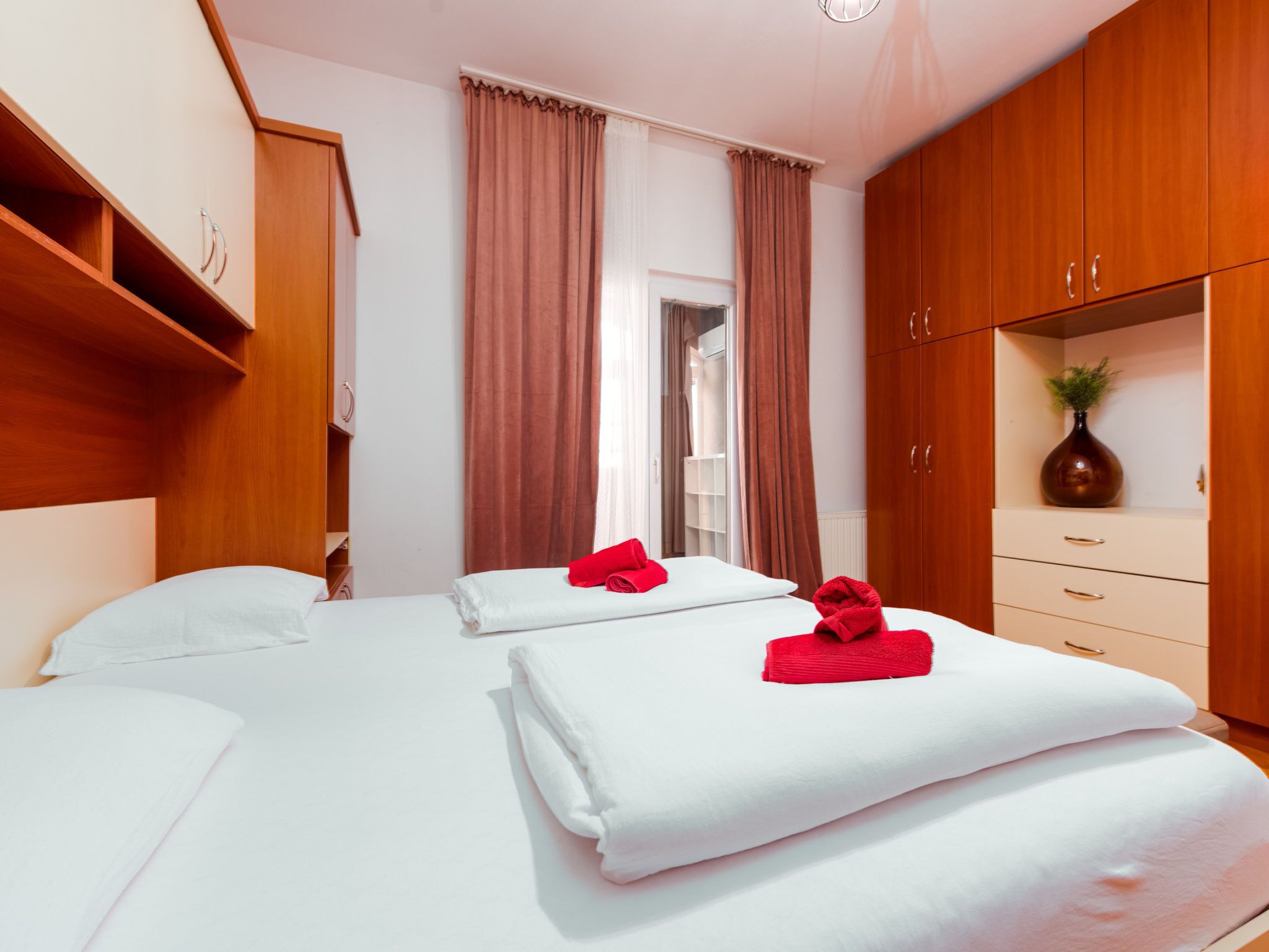 A hotel room with two beds, wooden wardrobe, and a bathroom visible through a door.
