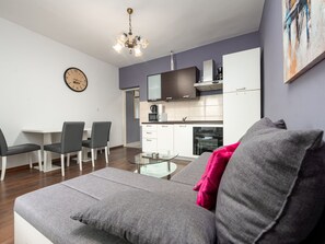 Ein modernes Wohnzimmer mit einem grauen Sofa, einem Glastisch und einem Essbereich mit weißem Tisch und Stühlen.