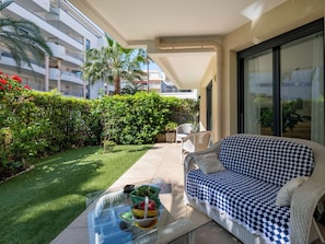 Ein Balkon mit Glastisch, gestreiftem Sofa und Blick auf ein Gebäude mit Balkonen und Grünpflanzen.