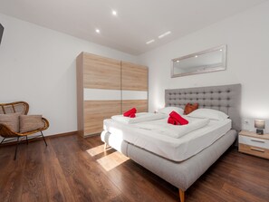 A modern bedroom with a large bed, a wooden wardrobe, a wicker chair, and a bedside table with a lamp. - Apartment  by Interhome (Biograd na Moru)