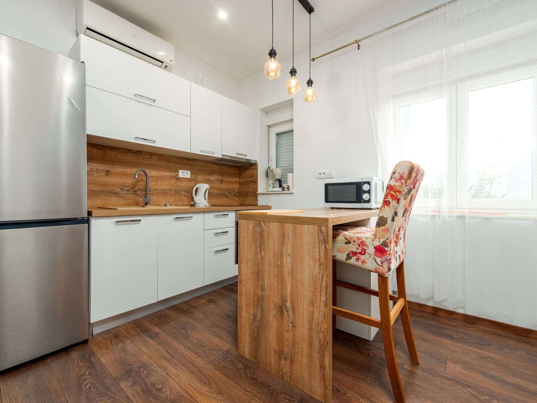 A modern kitchen with a wooden island, stainless steel appliances, and a floral chair.
