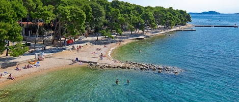 Una playa con agua cristalina, árboles y gente.