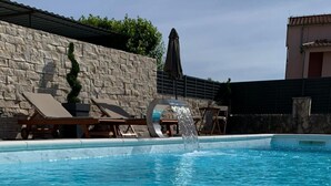 Ein Schwimmbecken mit klarem, blauem Wasser, Liegestühlen und einer Steinmauer.