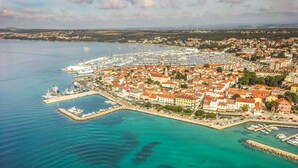 Eine Luftaufnahme einer Küstenstadt mit einem Yachthafen, Gebäuden am Wasser und freiem Blick auf das Meer.