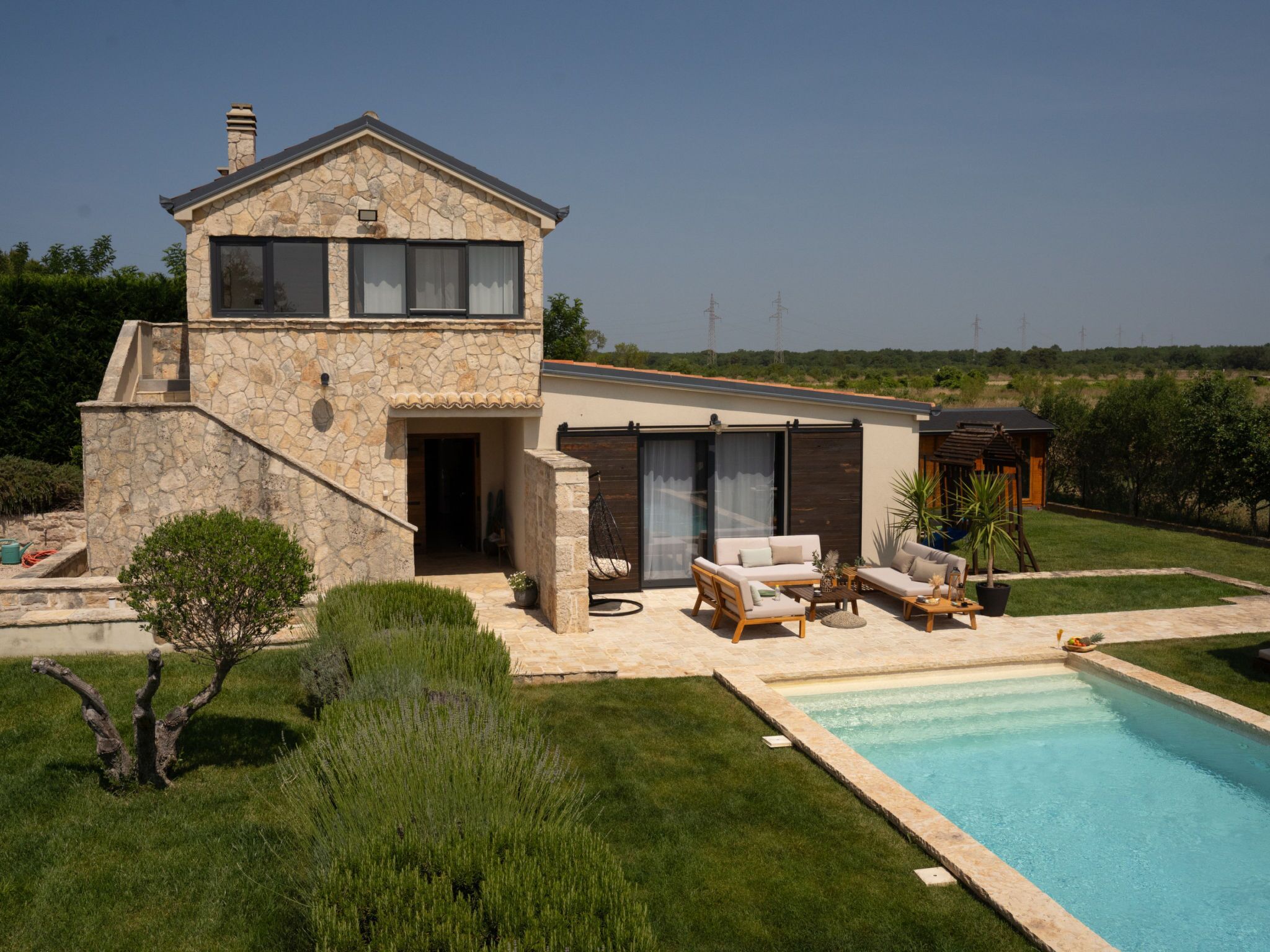 Una casa de dos plantas con fachada de piedra, piscina y mobiliario exterior.
